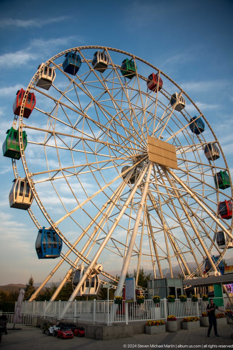 Ferris wheel at Kok Tobe photographed from below, showing colorful enclosed gondolas and metal spokes against the sky.