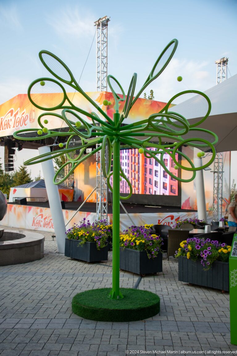 Green metal branching canopy above flower planters and a small stage area at Kok Tobe.