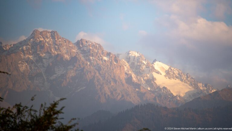 Panoramic view from Kok Tobe of the jagged Tian Shan mountain ridge with large white snowfields and glaciers.