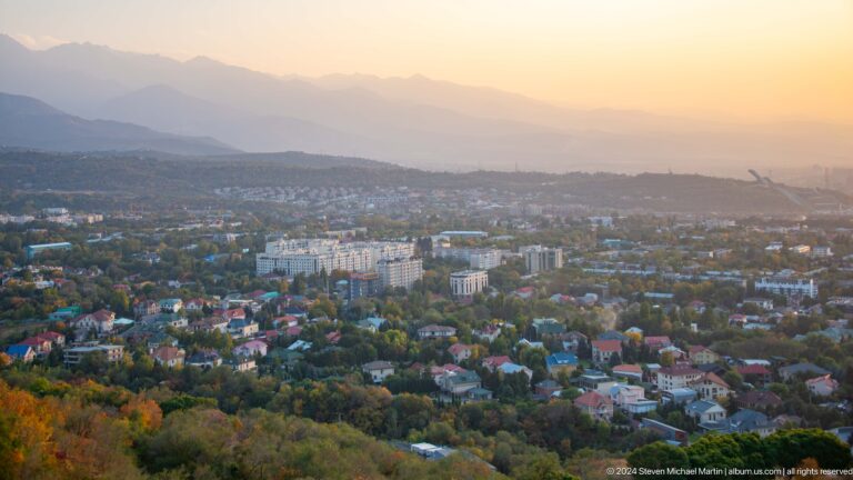 Elevated view from Kok Tobe over residential districts in western Almaty with hazy foothills and mountains in the distance.