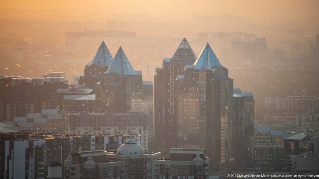Telephoto view of distinctive peaked-roof towers in central Almaty seen through evening haze from Kok Tobe.
