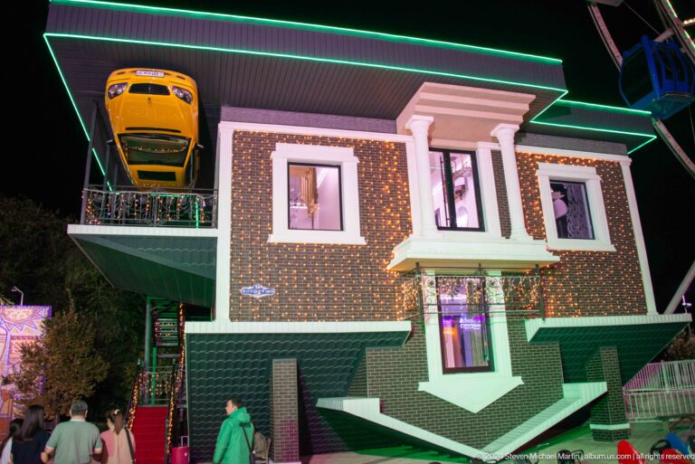 Upside-down house attraction at Kok Tobe at night, with inverted windows and porch edged in green lighting.