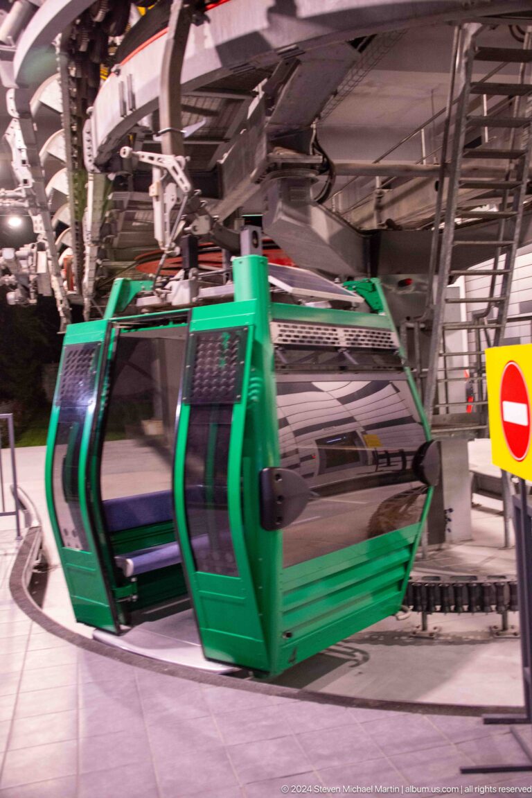 Green gondola cabin in the Kok Tobe cable-car station at night, beside a curved loading track and station machinery.