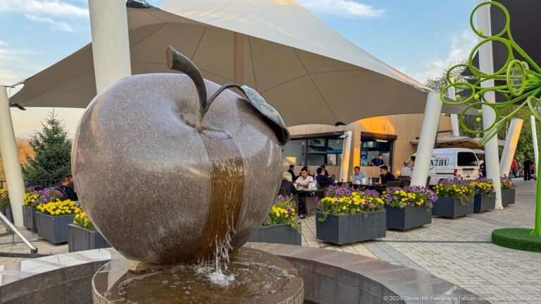 Polished stone apple fountain with a metal leaf, water flowing down its front into a circular basin at Kok Tobe in Almaty.