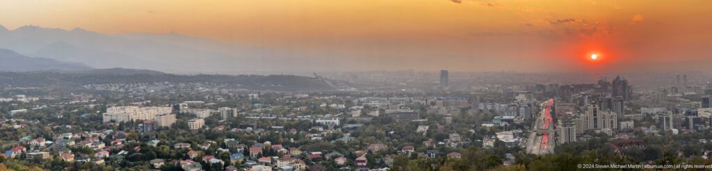 Elevated hazy view from Kok Tobe over Almaty’s low-rise residential neighborhoods with a single tall tower in the distance.