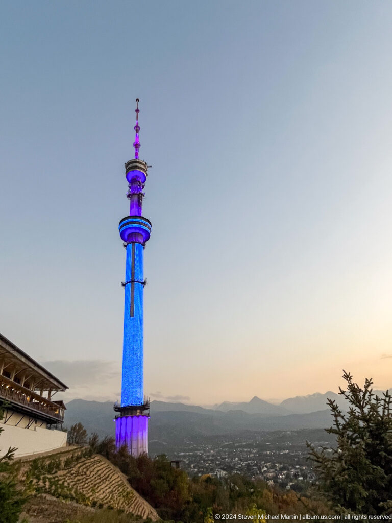 Almaty Television Tower lit in blue and purple against the evening sky, viewed from Kok Tobe.