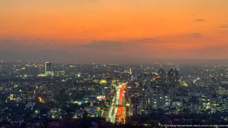 Elevated blue-hour view of Almaty from Kok Tobe, with a brightly lit avenue cutting through the darkening city.