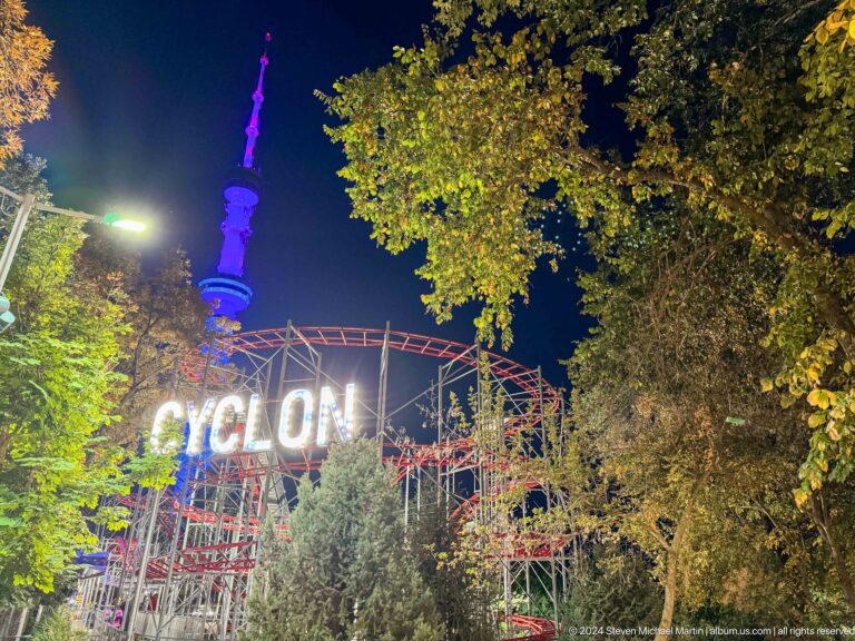 Illuminated Cyclon roller-coaster sign with red track and the Almaty Television Tower at night in Kok Tobe.