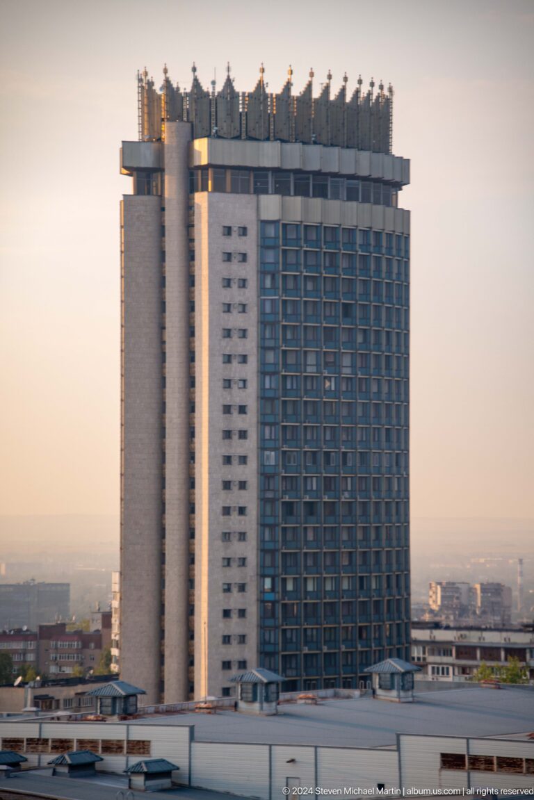 Telephoto view of a modern high-rise facade in Almaty with a regular dark window grid and a light vertical structural wall.