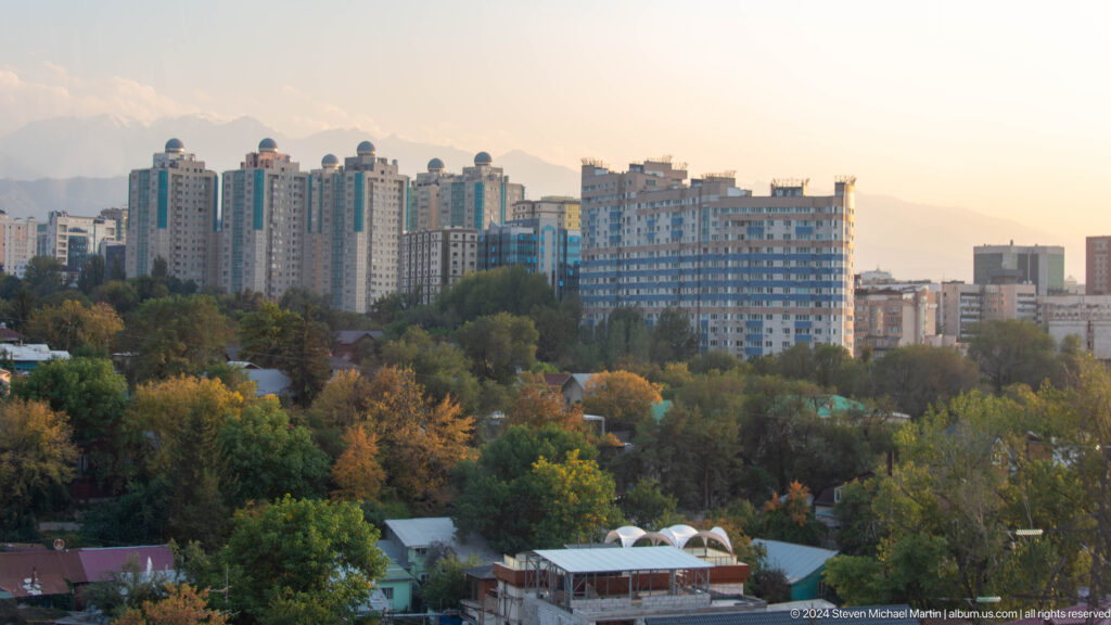 Panoramic view from Kok Tobe of Almaty apartment towers and low-rise neighborhoods with hazy Tian Shan mountains in the background.