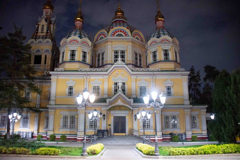 Illuminated rear or side facade with garden lamps at the colorful wooden Zenkov Cathedral in Almaty.