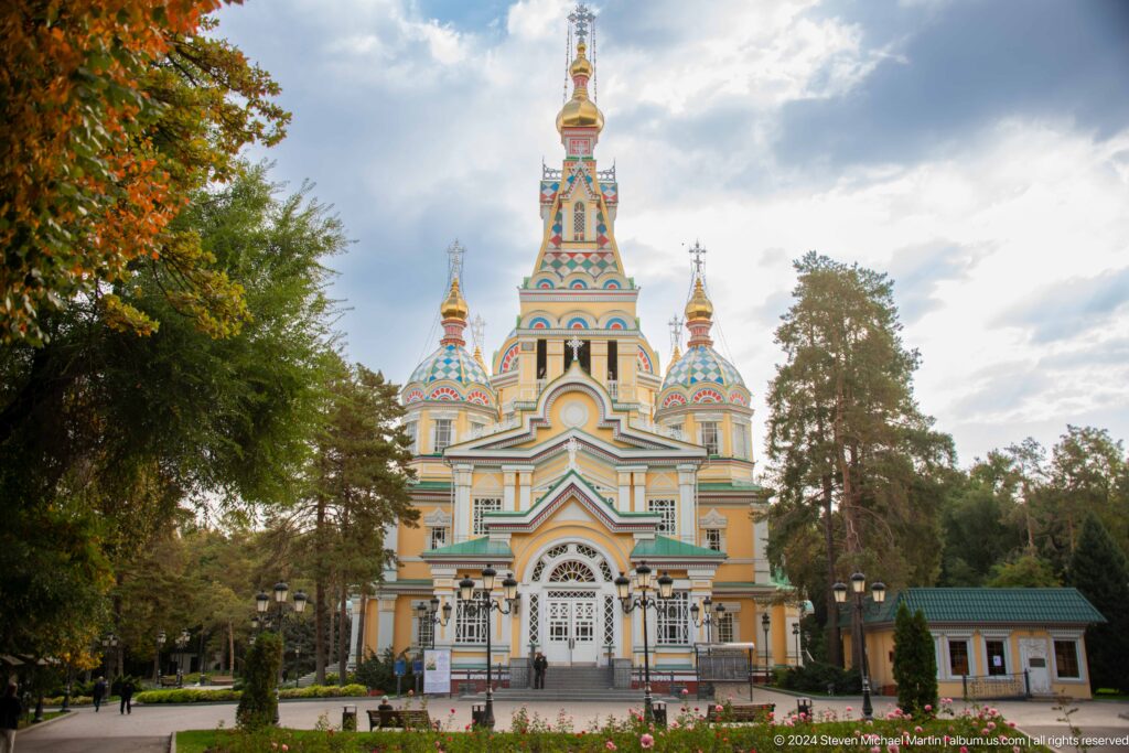 Daylight establishing view framed by autumn trees at the colorful wooden Zenkov Cathedral in Almaty.