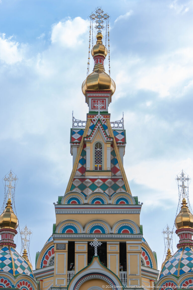 Bell tower against pale sky at the colorful wooden Zenkov Cathedral in Almaty.