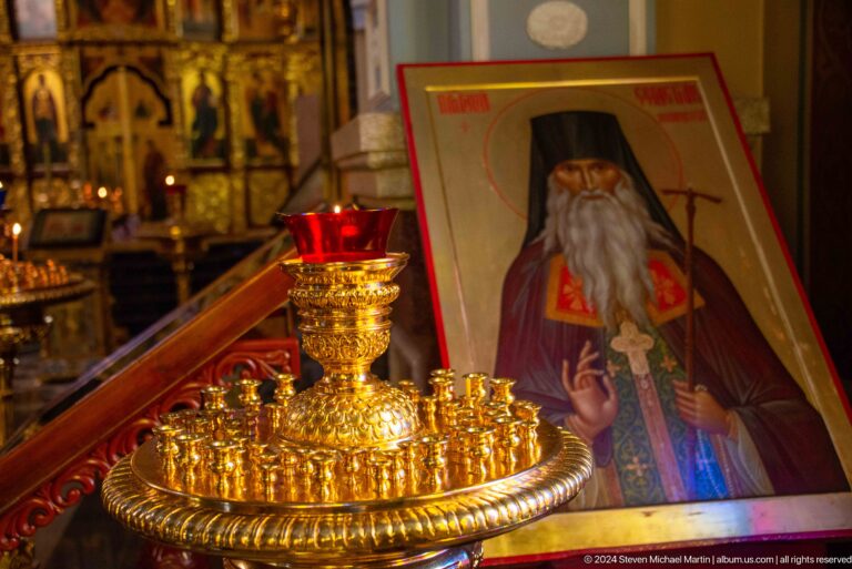 Votive candle stand before an icon inside Zenkov Cathedral, with Orthodox religious decoration.