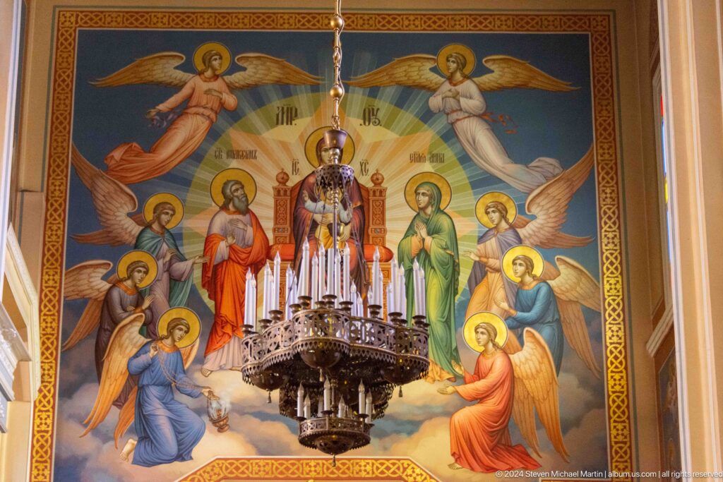 Chandelier before mural of saints inside Zenkov Cathedral, with Orthodox religious decoration.