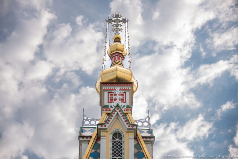 Bell tower rising into clouded sky at the colorful wooden Zenkov Cathedral in Almaty.