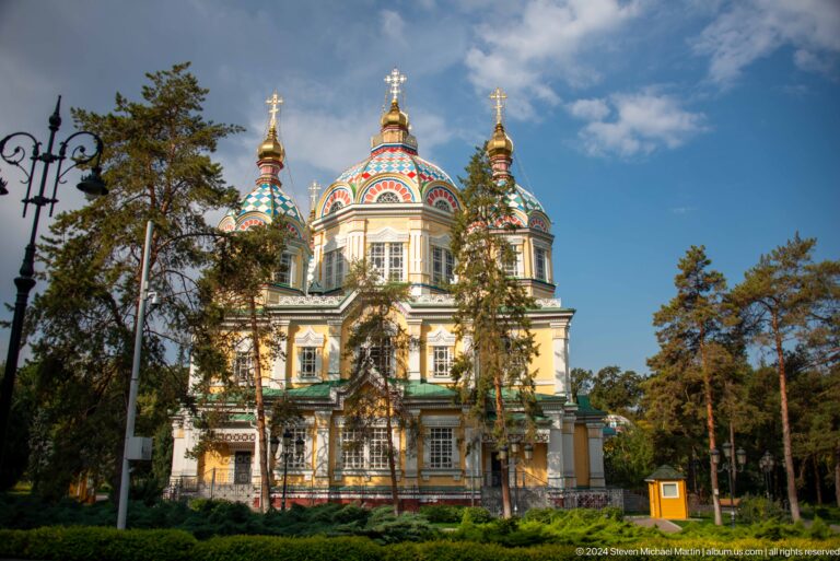 Wide daytime exterior among trees at the colorful wooden Zenkov Cathedral in Almaty.