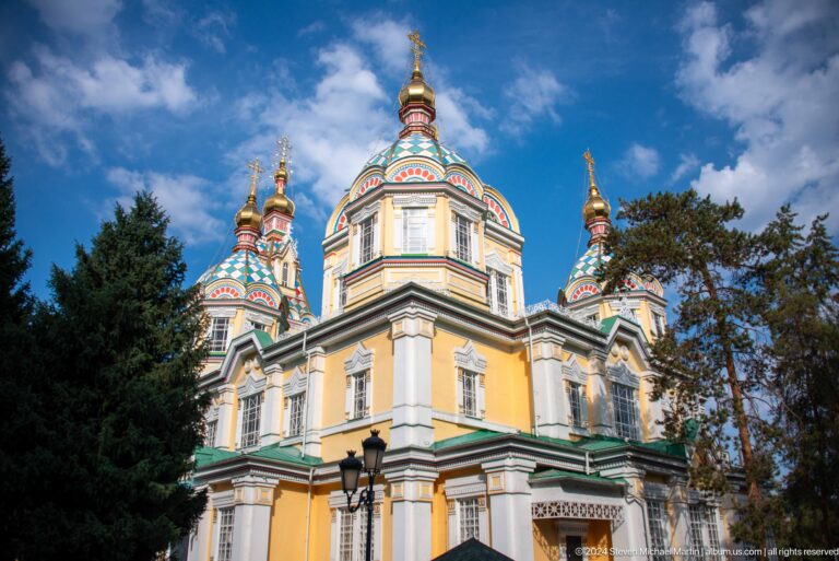 Low-angle daylight facade and domes at the colorful wooden Zenkov Cathedral in Almaty.