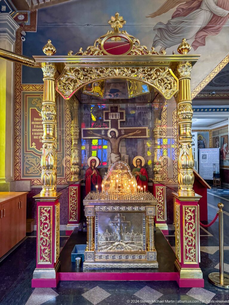 Crucifix shrine and votive candles inside Zenkov Cathedral, with Orthodox religious decoration.