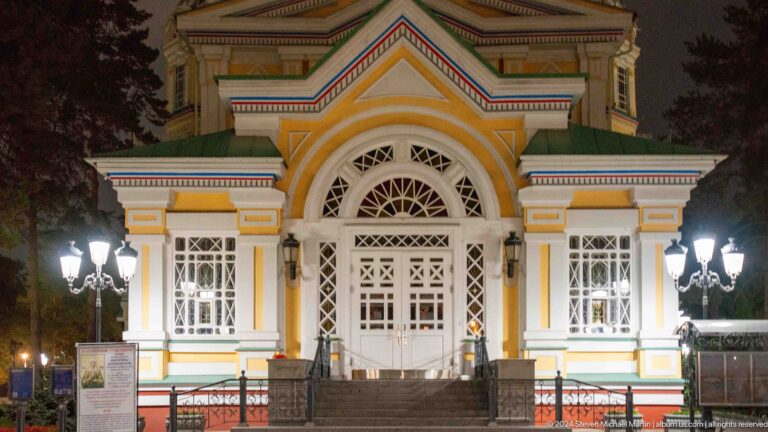 Illuminated entrance porch and white doors at the colorful wooden Zenkov Cathedral in Almaty.