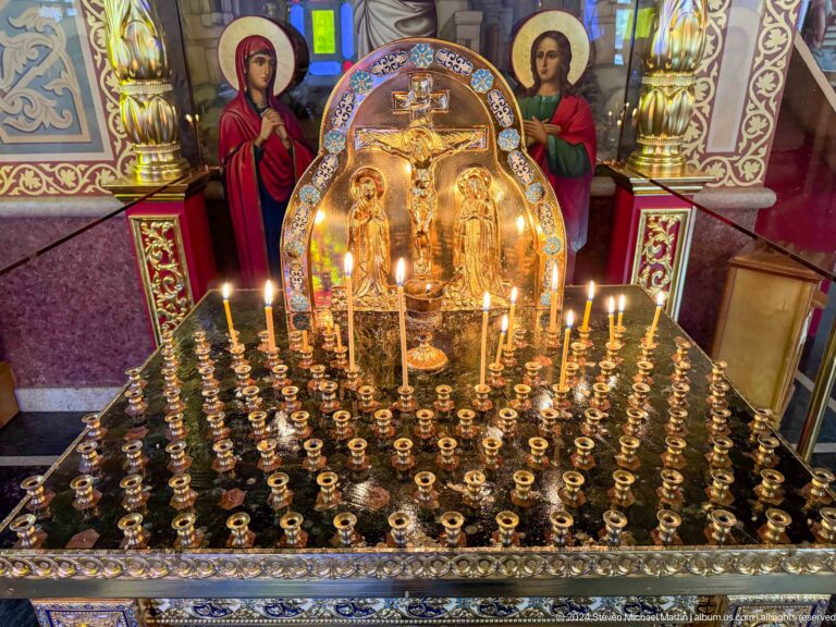 Large brass votive candle stand inside Zenkov Cathedral, with Orthodox religious decoration.