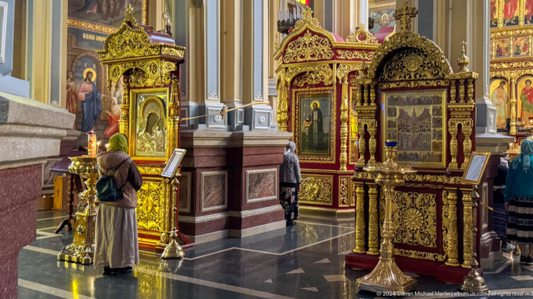 Gilded icon stands with worshippers inside Zenkov Cathedral, with Orthodox religious decoration.