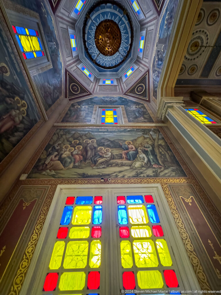 Large biblical mural above stained glass inside Zenkov Cathedral, with Orthodox religious decoration.