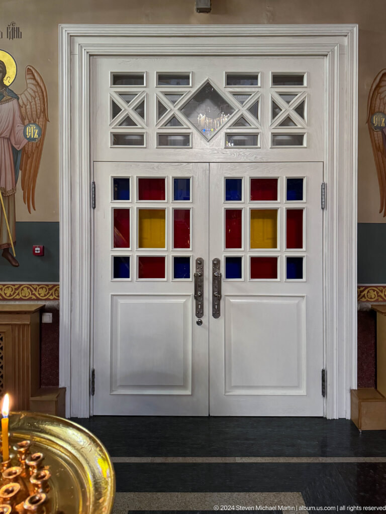 White interior doors with colored glass inside Zenkov Cathedral, with Orthodox religious decoration.