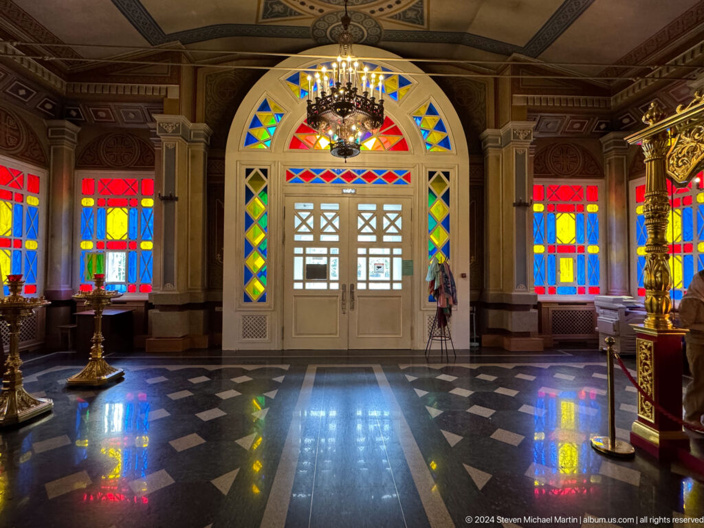 Entrance hall with stained glass and reflective floor inside Zenkov Cathedral, with Orthodox religious decoration.