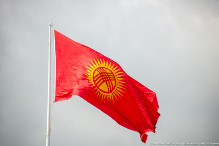 Red Kyrgyz flag billowing against clouds in Bishkek, Kyrgyzstan.