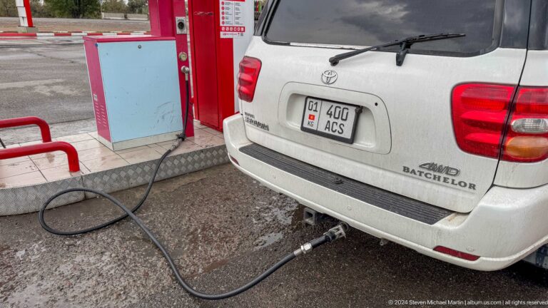 White SUV beside red fuel pump in Bishkek, Kyrgyzstan.