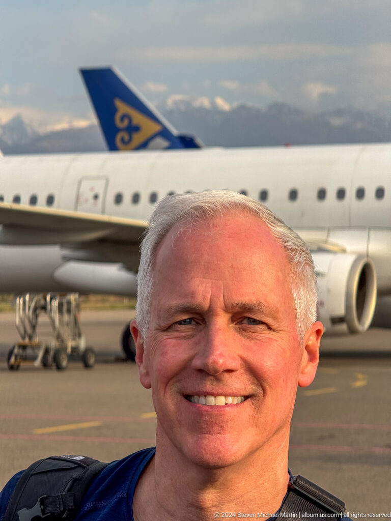 Smiling gray-haired man with aircraft behind in Bishkek, Kyrgyzstan.