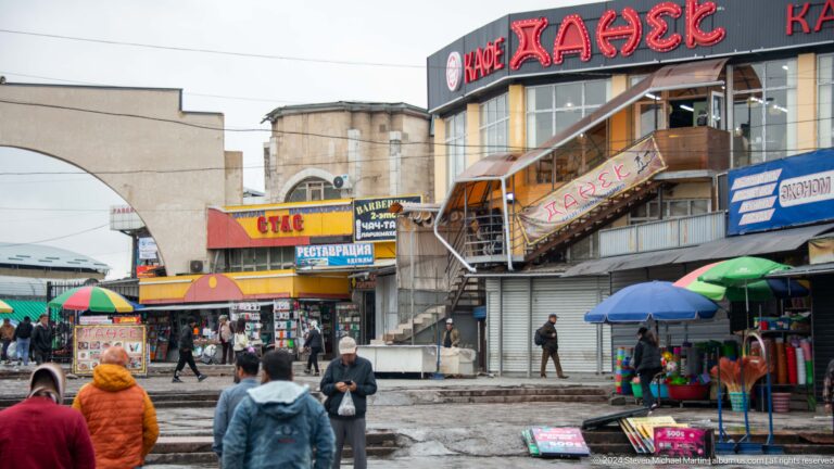 Busy market entrance beneath Cyrillic signs in Bishkek, Kyrgyzstan.