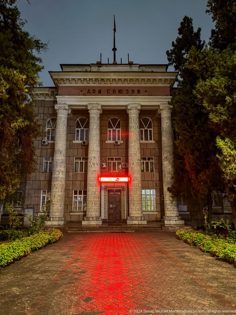 Columned institutional facade with red sign in Bishkek, Kyrgyzstan.