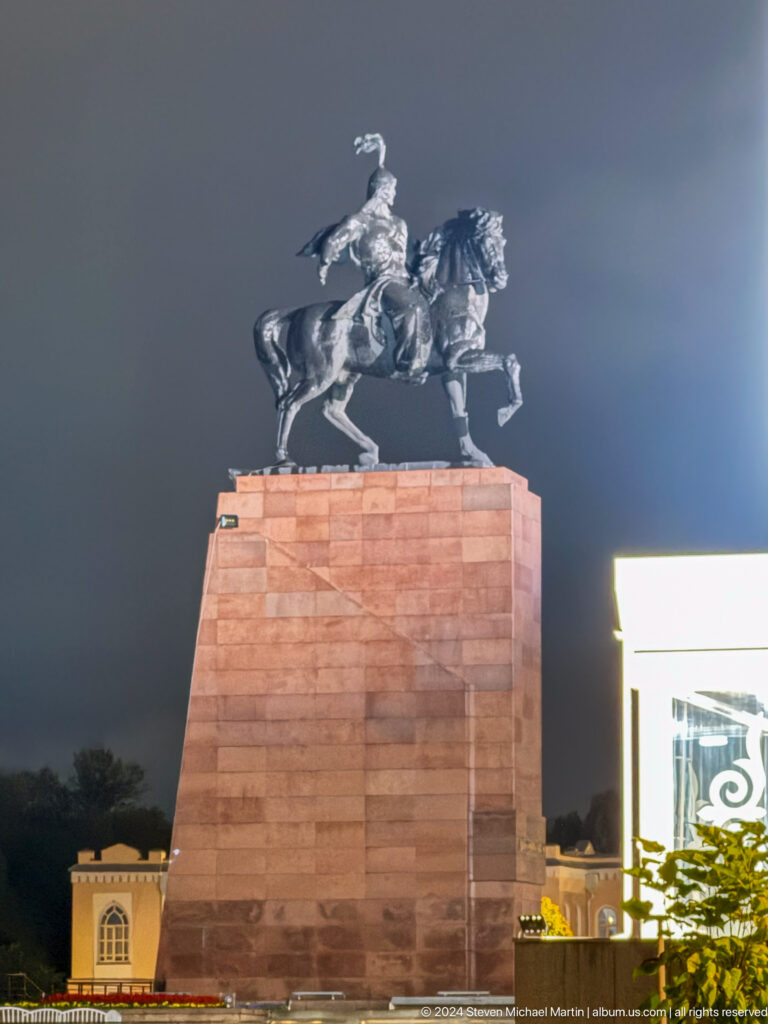 Equestrian statue on red stone pedestal at night in Bishkek, Kyrgyzstan.