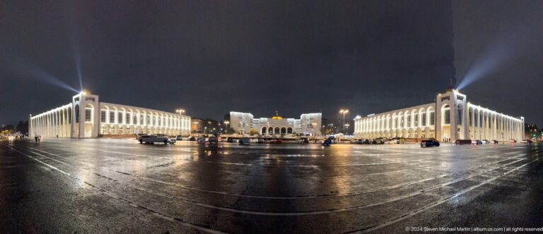 Wide rain-wet square with illuminated buildings in Bishkek, Kyrgyzstan.