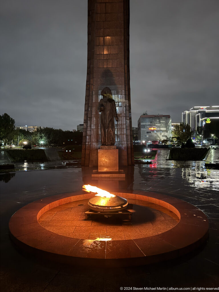 Standing statue beside eternal flame at night in Bishkek, Kyrgyzstan.