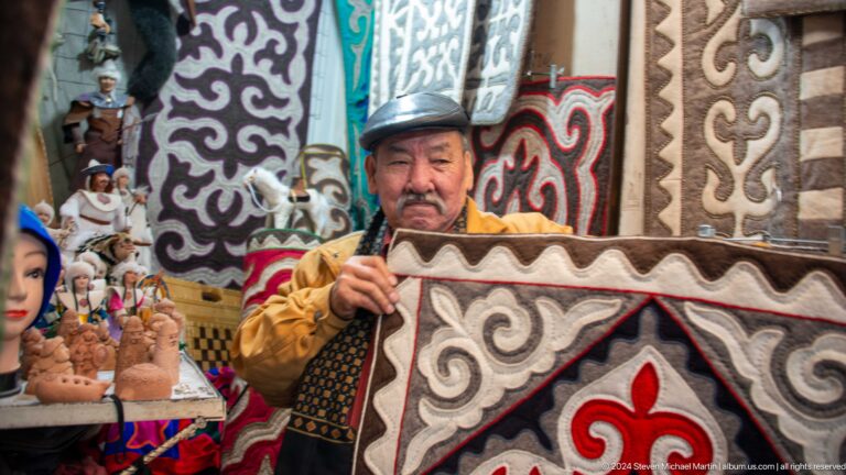 Male vendor holding a patterned felt rug in Bishkek, Kyrgyzstan.