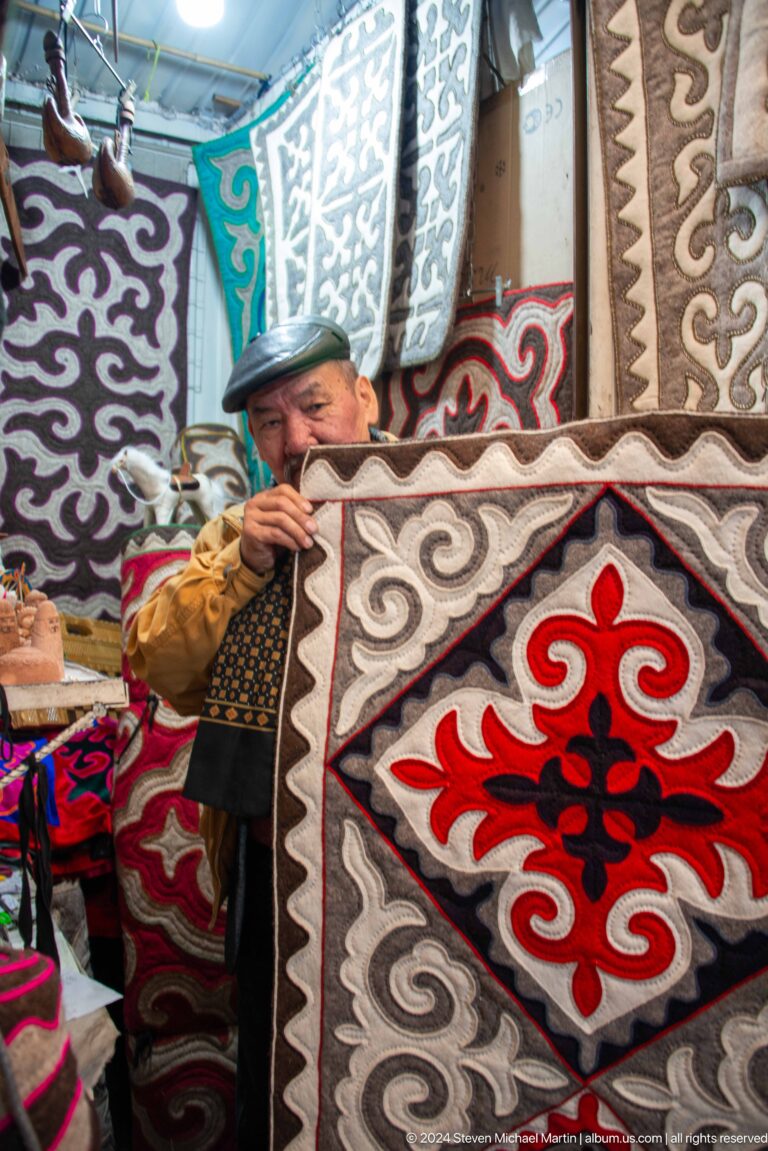 Vendor lifting red and gray felt rug in Bishkek, Kyrgyzstan.