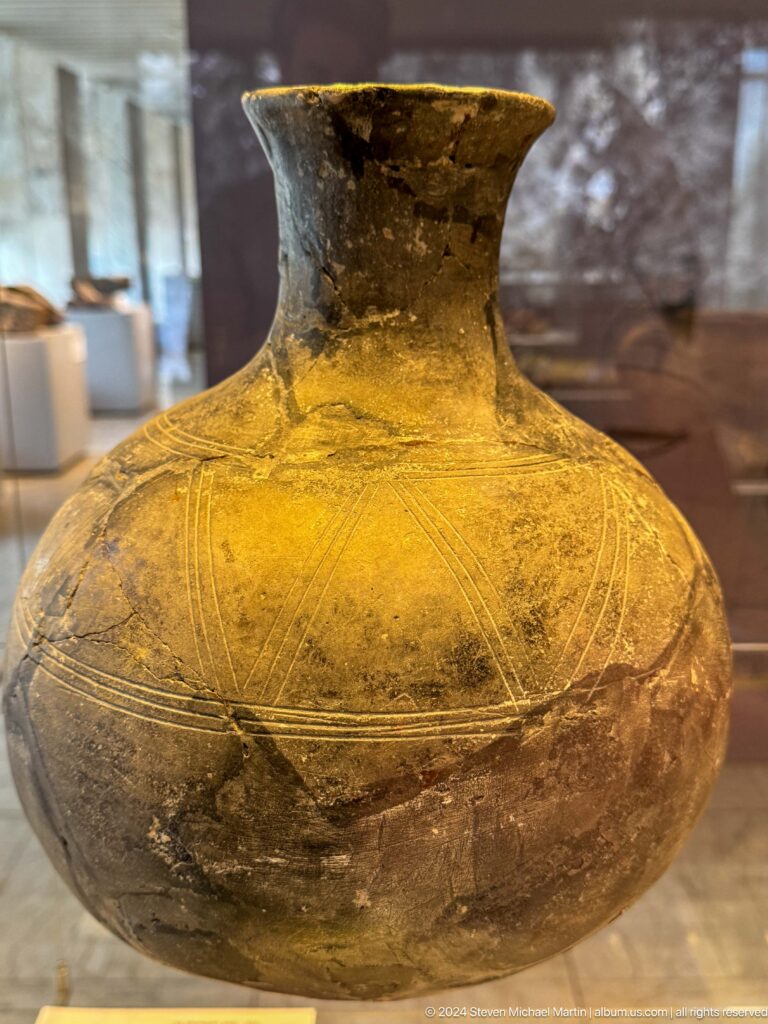 Gold-toned globular vessel engraved with fine bands.