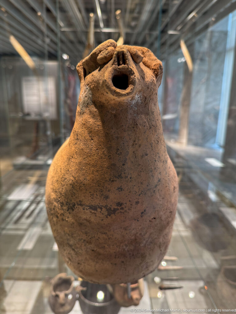 Small rough clay vessel with bulbous lower body and narrow opening.