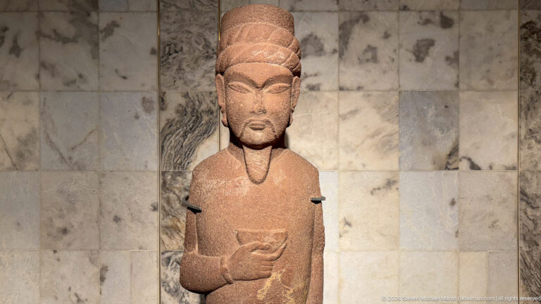 Terracotta female figurine standing against a display panel.