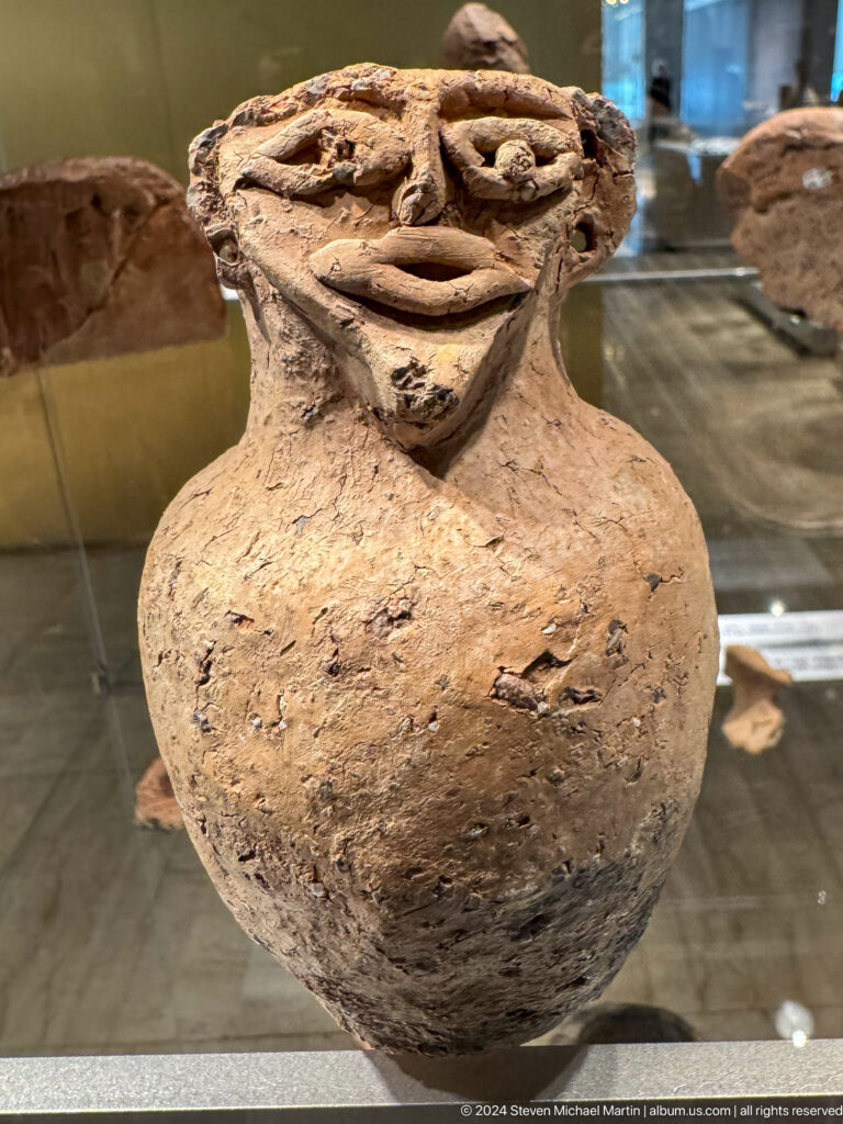 Rounded clay vessel modeled with a human face and shoulders.