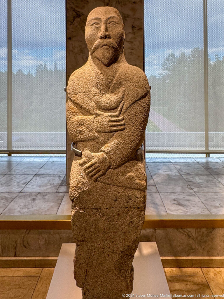 Upright carved stone torso with hands crossed at waist.