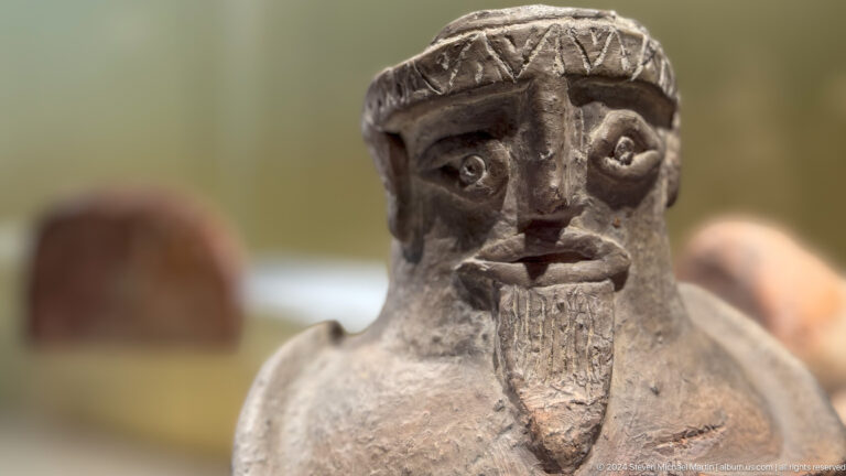 Close view of carved stone head with large eyes and beard.