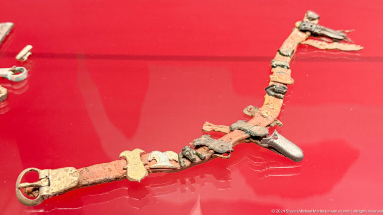 Curving assemblage of small bone or metal fittings on red fabric.