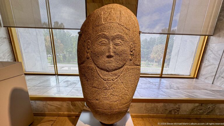 Tall oval stone figure with smiling face and cap.