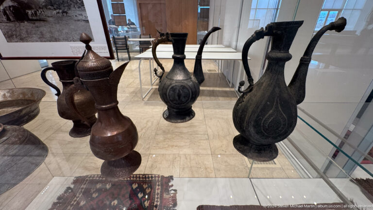 Group of dark metal ewers with tall handles and spouts.