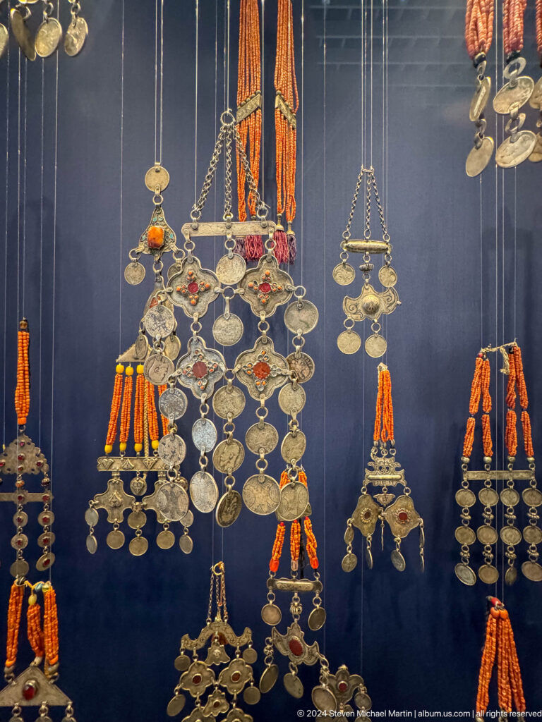 Large silver chest ornament with coins and orange tassels.