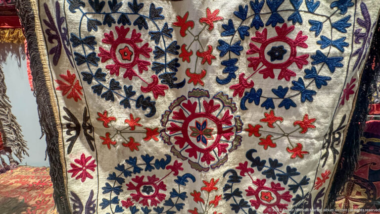 Large white textile embroidered with red blue and green flowers.